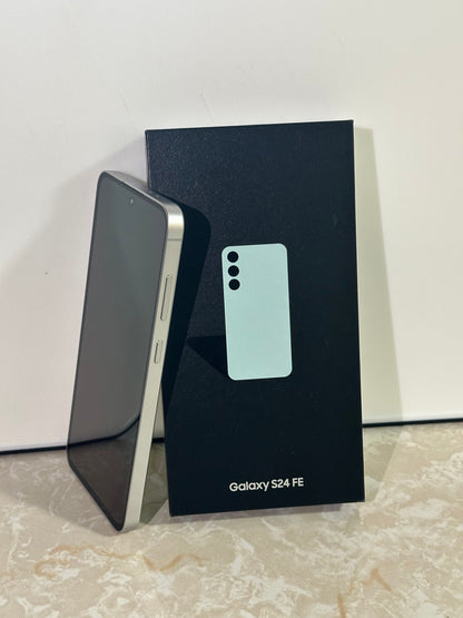 Samsung Galaxy S24 FE phone next to its packaging on a light surface.